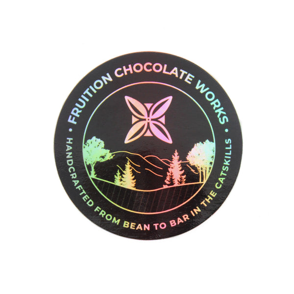 Round sticker with a black background, and the text and image are holographic. Text around the outside says "fruition chocolate works, handcrafted from bean to bar in the catskills", and the center is a drawing of mountains and trees